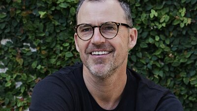 Coloured profile image of man wearing glasses smiling and looking past camera