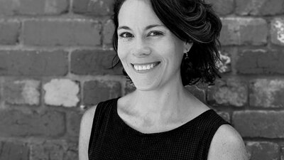 Black and white profile image of woman smiling and looking at camera, hair is up