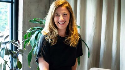 Colour photo of woman with mid length hair sitting and smiling at camera