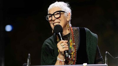 A woman with short grey hair and glasses holding a microphone on stage
