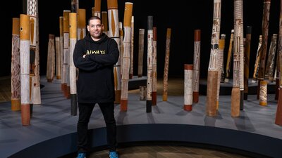 A man standing in a gallery space with indigenous poles