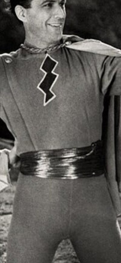 black and white image of man dressed as a superhero smiling, with two people on either side