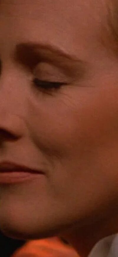 Close up of woman dressed in tuxedo with eyes closed pressed against chin of another person