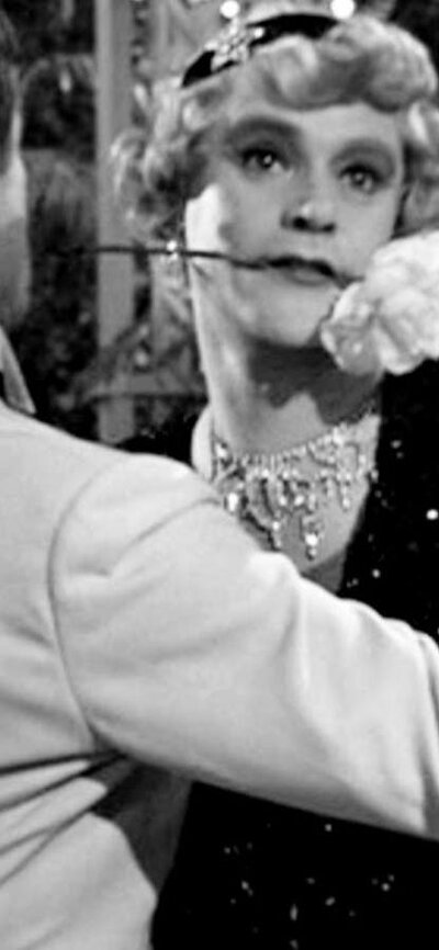 Black and white still of two men dancing, one dressed as a woman with a flower in his mouth