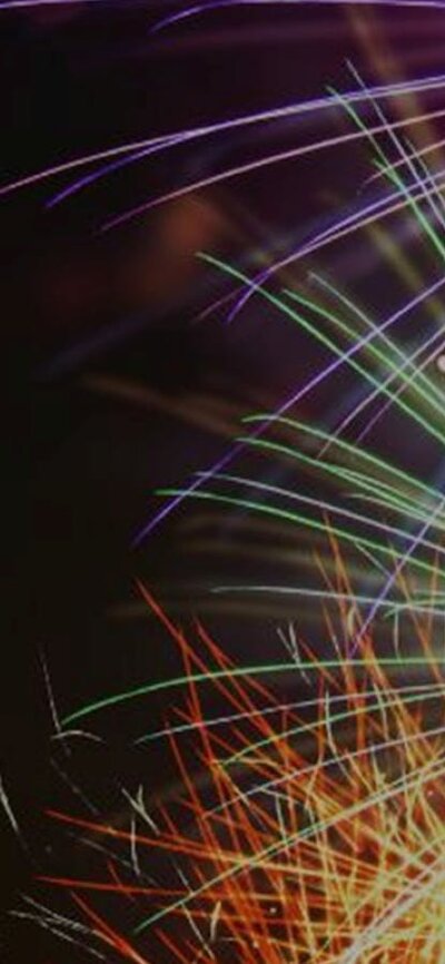 Celebration - Fireworks image Magenta, green, yellow, orange fireworks exploding on right-hand side against a black background.