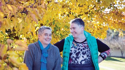 Two women standing happily under a tree with yellow leaves during Autumn in Canberra