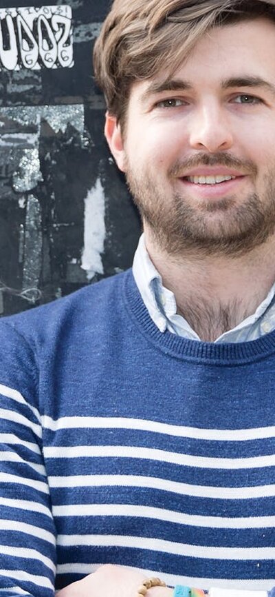 A man with brown hair and beard stands in front of a YES for Marriage Equality poster