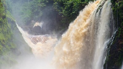 Kayakers under a large waterfall