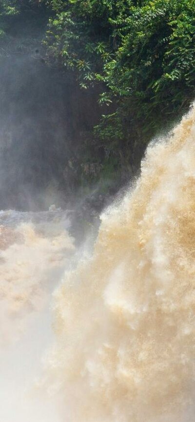Kayakers under a large waterfall