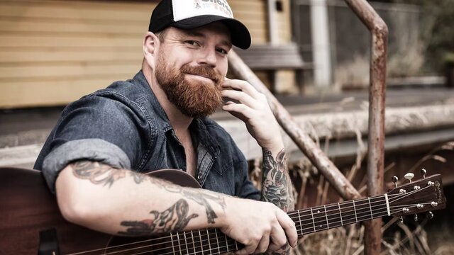 Photo of the artist, Andrew Swift Man sitting on a step with a guitar
