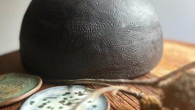 dark round ceramic vessel on a brown table with small blue and green plates