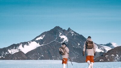 Expeditioners walking towards Mount Henderson, 1960. © George Cresswell/AAD Two hikers trekking across a snow-covered landscape with a mountain in the background.