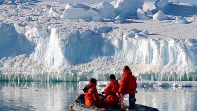 Three people in a small inflatable boat looking at the large ice formation in front of them.