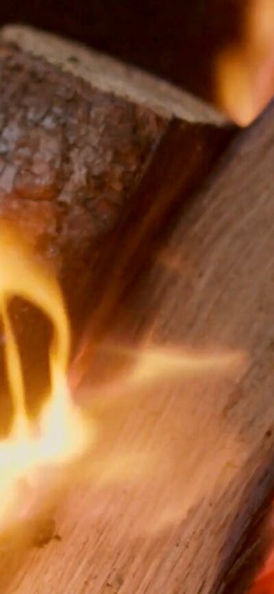 Flames dance brightly against a dark metal firepit, glowing in the low light of the evening