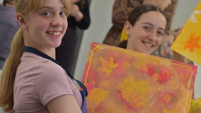 Two smiling girls holding up autumn leaf paintings
