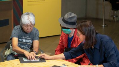 A photograph of 2 participants of Art by Description and a staff member using tactile resources