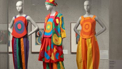 A photograph of three colourful, patchwork outfits on mannequins in a gallery