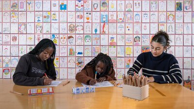 Three young girls sit together at a table, colouring in templates to create their own mini trains
