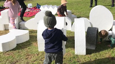 A photograph of children playing outdoors on a sculpture of white abstract shapes