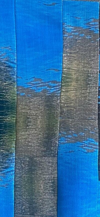 The Long Con (detail) by Helen Heslop A quilt made up of thin strips of fabric, with an abstracted motif of ripples in water.