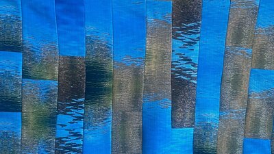 The Long Con (detail) by Helen Heslop A quilt made up of thin strips of fabric, with an abstracted motif of ripples in water.