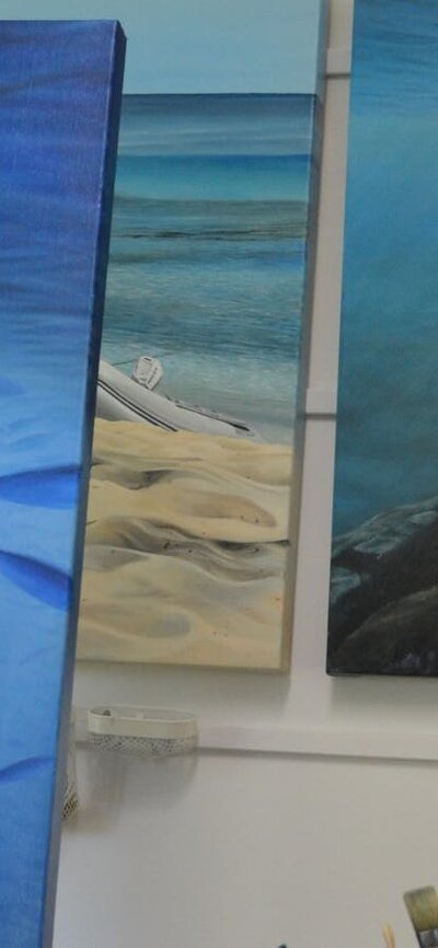Jeanette Muirhead paints an underwater seascape in her studio, with paintings, and brushes nearby.