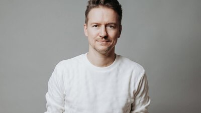 Person with brown hair and facial hair wearing white long sleeve shirt