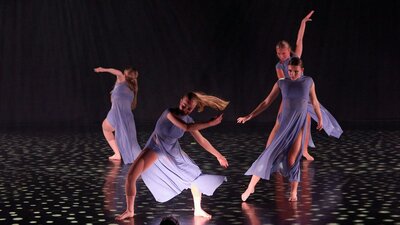 A group of dancers in flowing lavender costumes performing a synchronized routine.