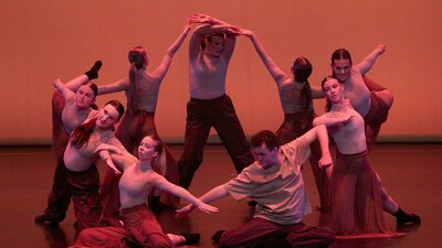 A group of dancers performing a synchronized contemporary piece, with warm lighting.