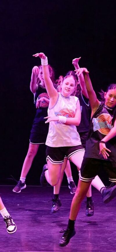 A group of young dancers performing a synchronized routine, wearing basketball inspired costumes.