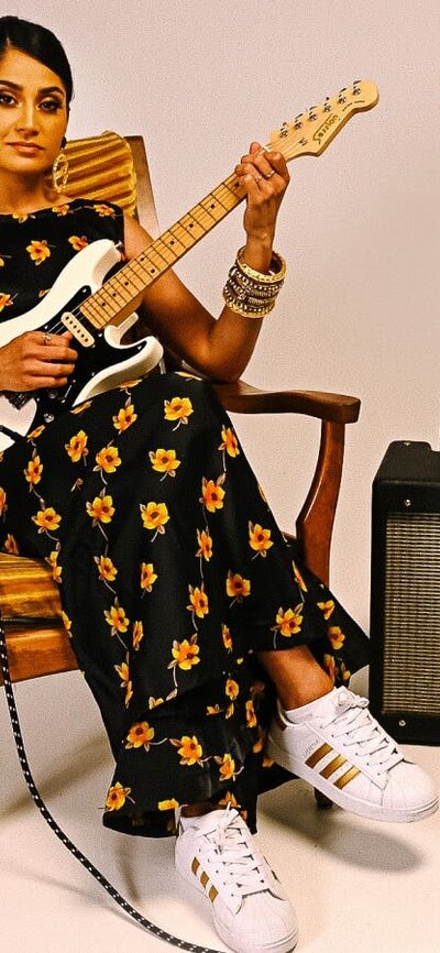 Performer Parvyn sitting on a chair playing the electric guitar