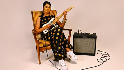 Performer Parvyn sitting on a chair playing the electric guitar