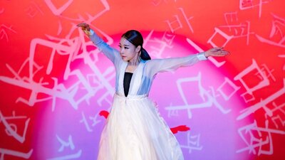 Korean dancer performing on stage with a red and pink backdrop behind her
