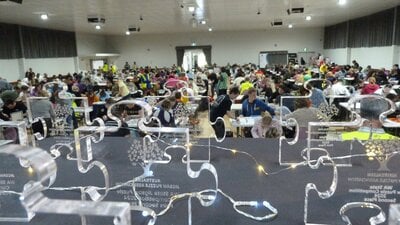 Puzzle Competition in progress A room full of puzzlers with awards in the foregrounf