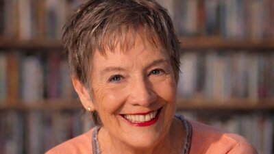 A smiling, mature woman with short, gray hair, looking directly at the camera in front of a blurred