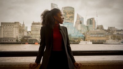 Natasha Brown A woman wearing a black blazer, staring into the distance with the city view behind her.