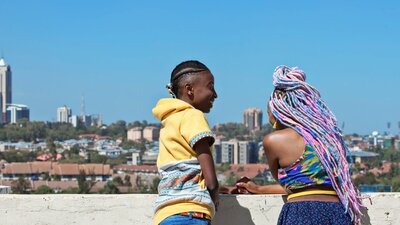 Two figures stand with their backs to the camera, one figure's head is turned and smiling