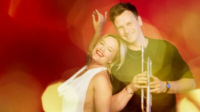 Rachel Mink - Soprano and Alex Raupach - Trumpet pose in front of a Christmas red background
