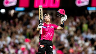 A Sydney Sixers batter raises a bat and helmet after scoring a century in a BBL match.