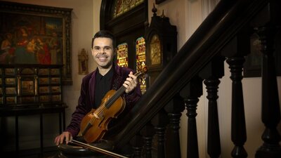 A violinist on a staircase in a grand old house.