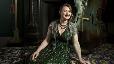 A double bass player seated n the floor in an elegant green dress.