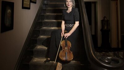 A viola player seated on a grand staicase in an elegant black dress