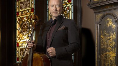 A cellist standing upright holding his instrument.