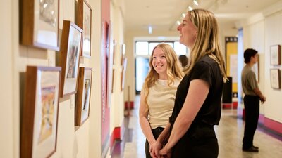 Two women view artwork in gallery.