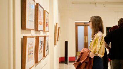 Woman views framed political cartoon in gallery.