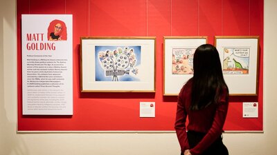 Woman views framer political cartoon in gallery.