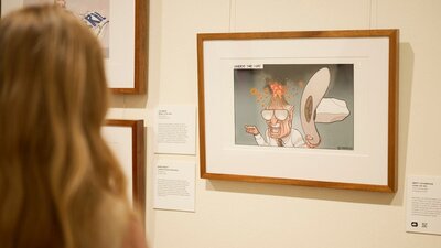 Woman views framer political cartoon in gallery.