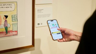 Phone shows audio description of political cartoon in gallery.