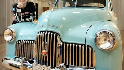 A woman poses on a vintage Holden car in an exhibition