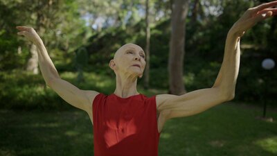 Bald woman wearing red dress with bare arms held high